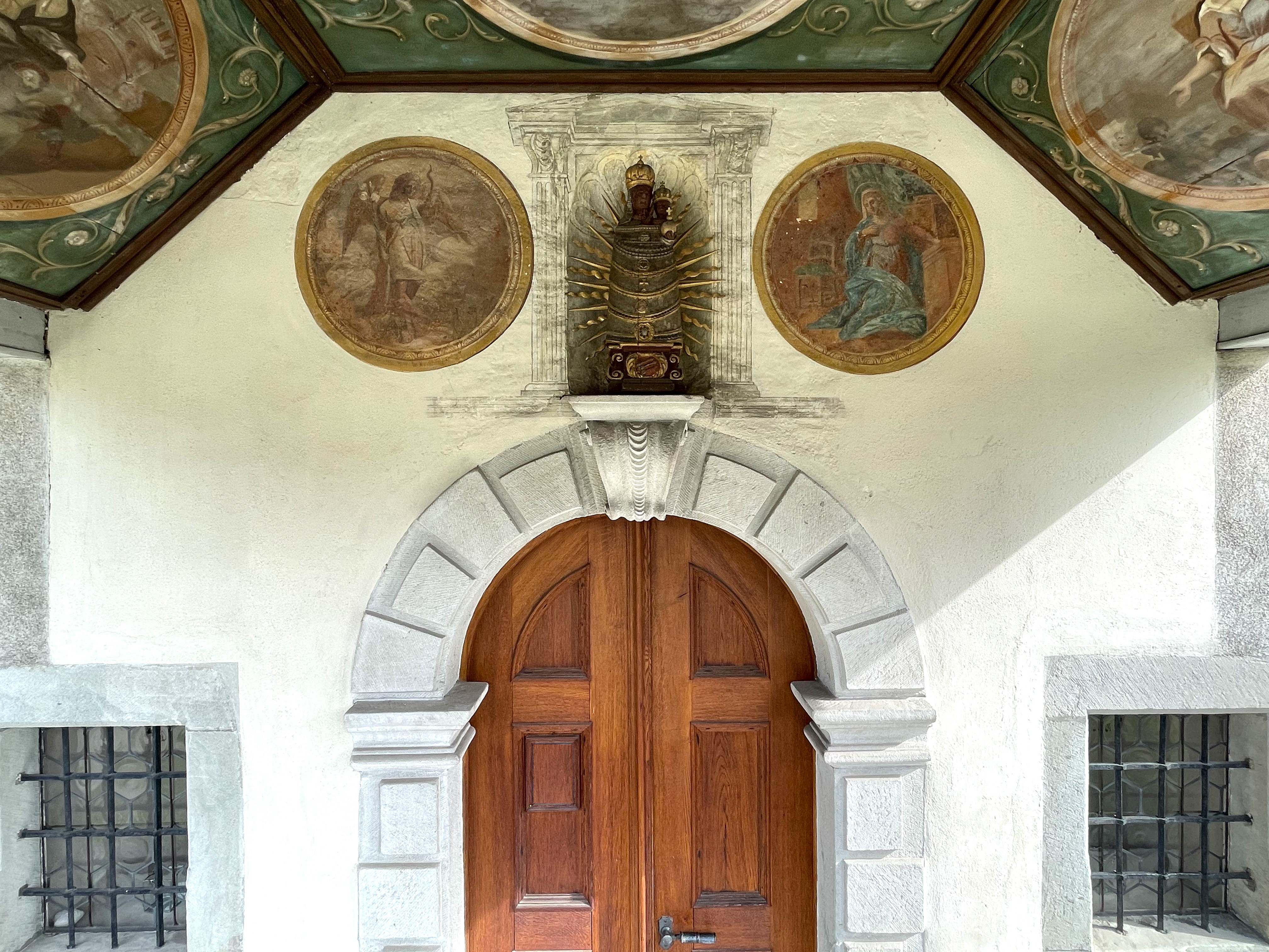 Eingangstür aus Holz mit Malereien und Marienstatue